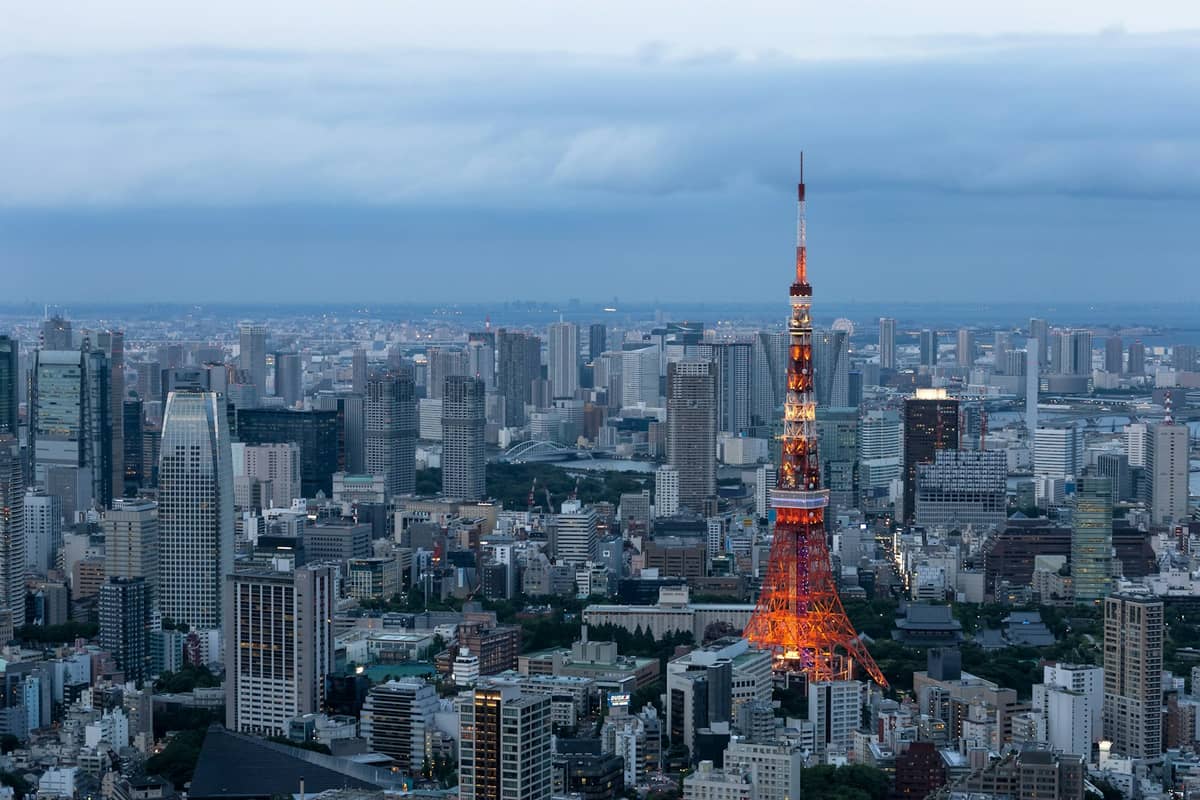 Aerial view of Tokyo city skyline with Tokyo Tower illuminated at dusk and clouds in the background.