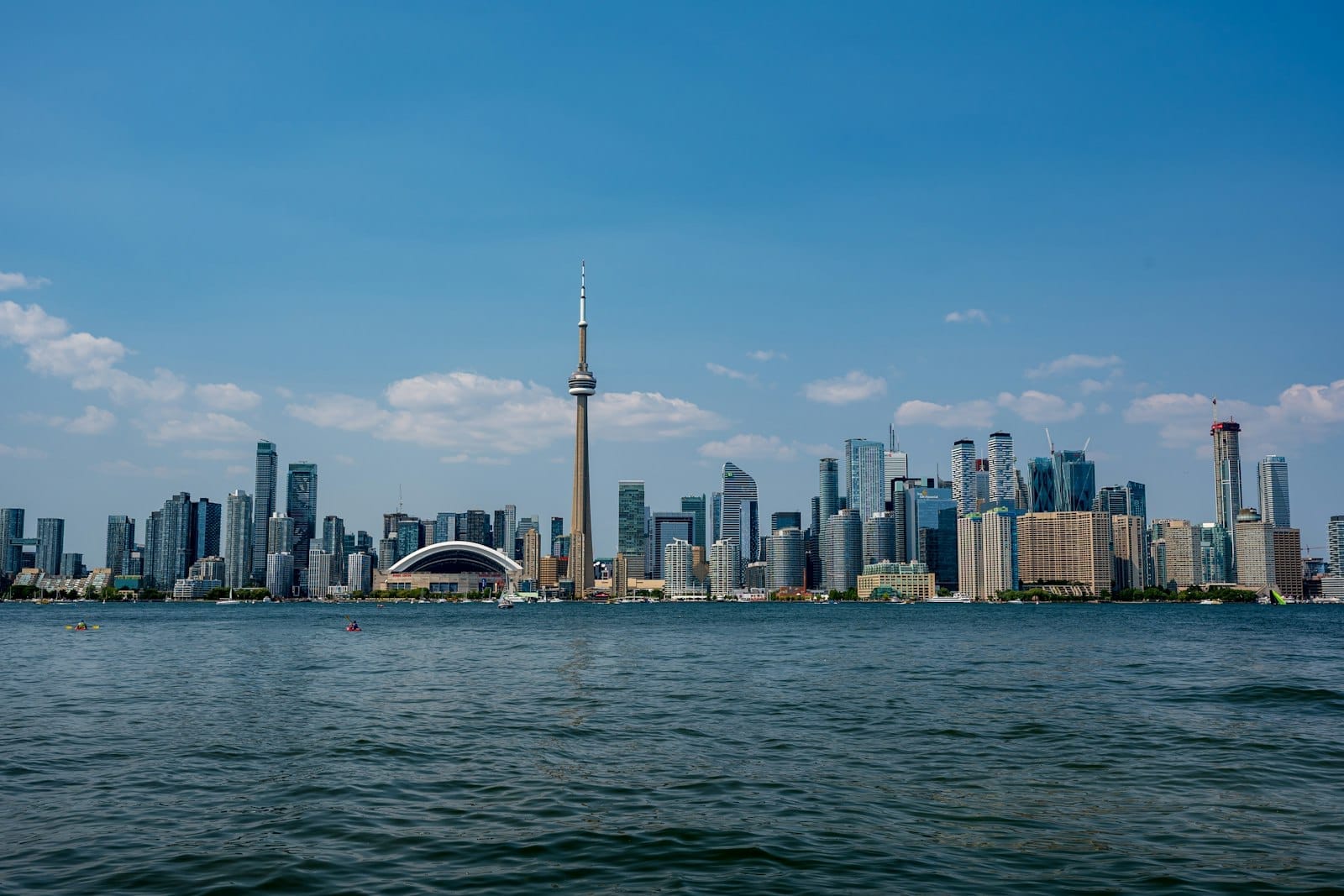 Horizonte de Toronto com a CN Tower em um dia ensolarado, visto do lado da água com céu azul e poucas nuvens.