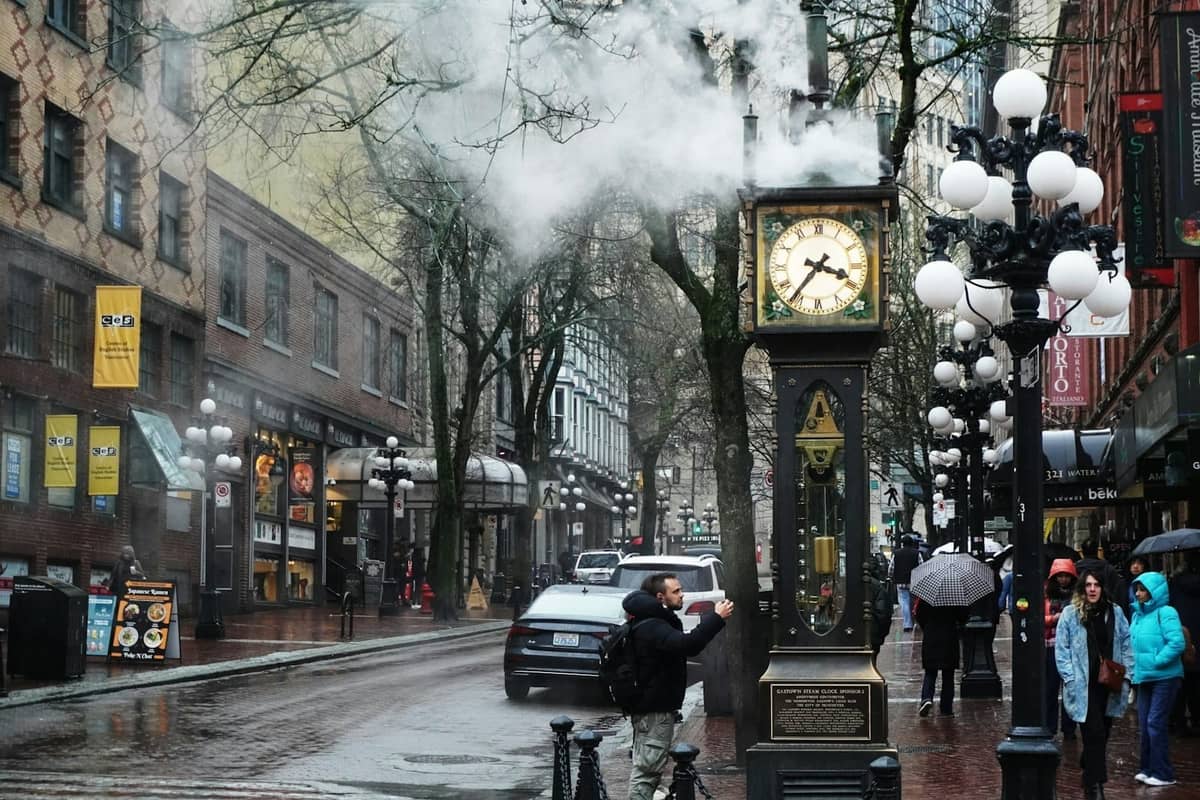 Gastown Steam Clock in Vancouver an einem regnerischen Wintertag mit Menschen mit Regenschirmen und nassen Straßen.