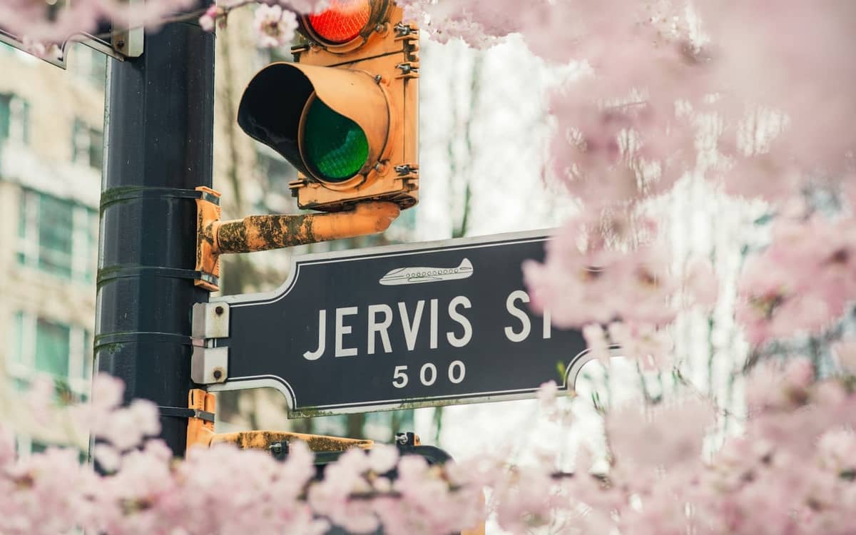 Straßenszene in Vancouver mit dem Schild Jervis St. und einer Ampel, umgeben von blühenden Kirschblüten im Frühling.