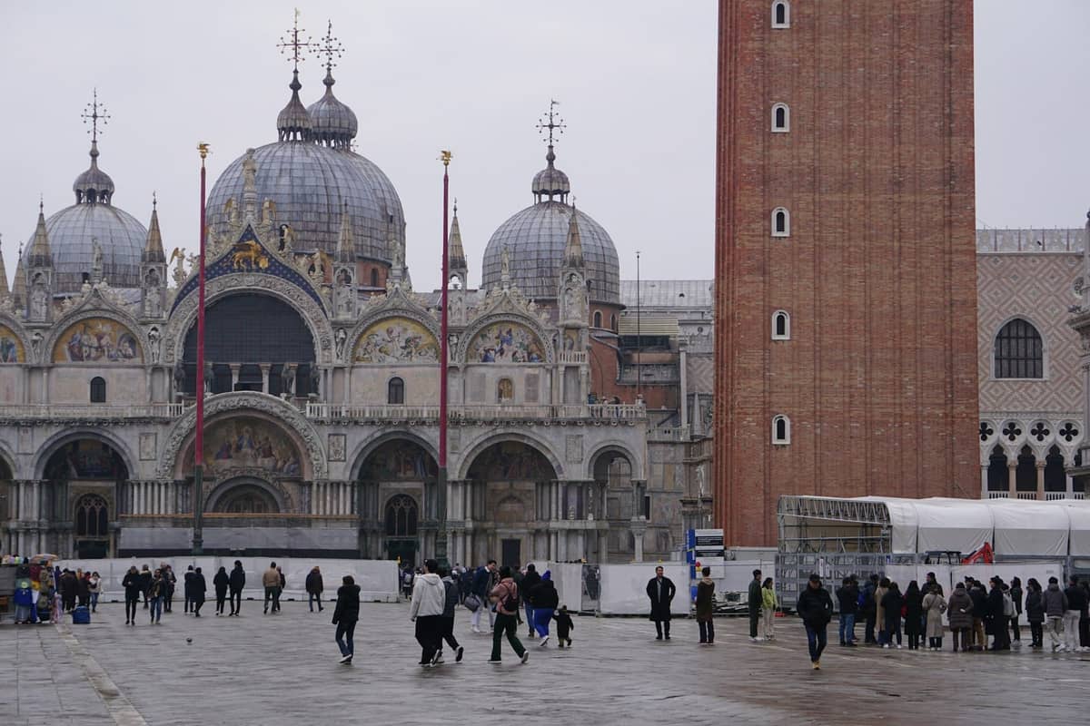 Die Markusbasilika und der Campanile in Venedig an einem grauen, feuchten Tag mit Menschen, die über den nassen Platz gehen