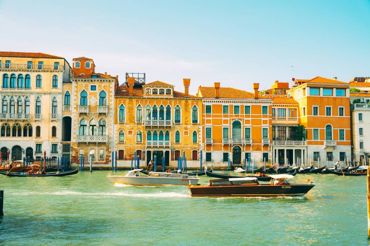 Venezianischer Kanal mit bunten historischen Gebäuden und Booten unter hellem Frühlingssonnenschein und klarem blauen Himmel