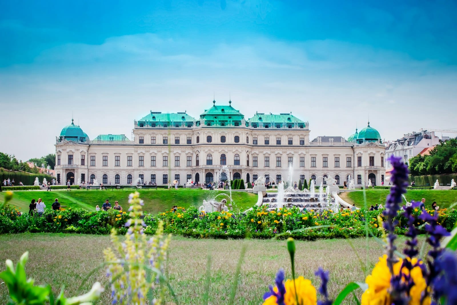 Il Palazzo del Belvedere a Vienna con vivaci fiori primaverili in fiore in primo piano e un cielo azzurro brillante sopra.