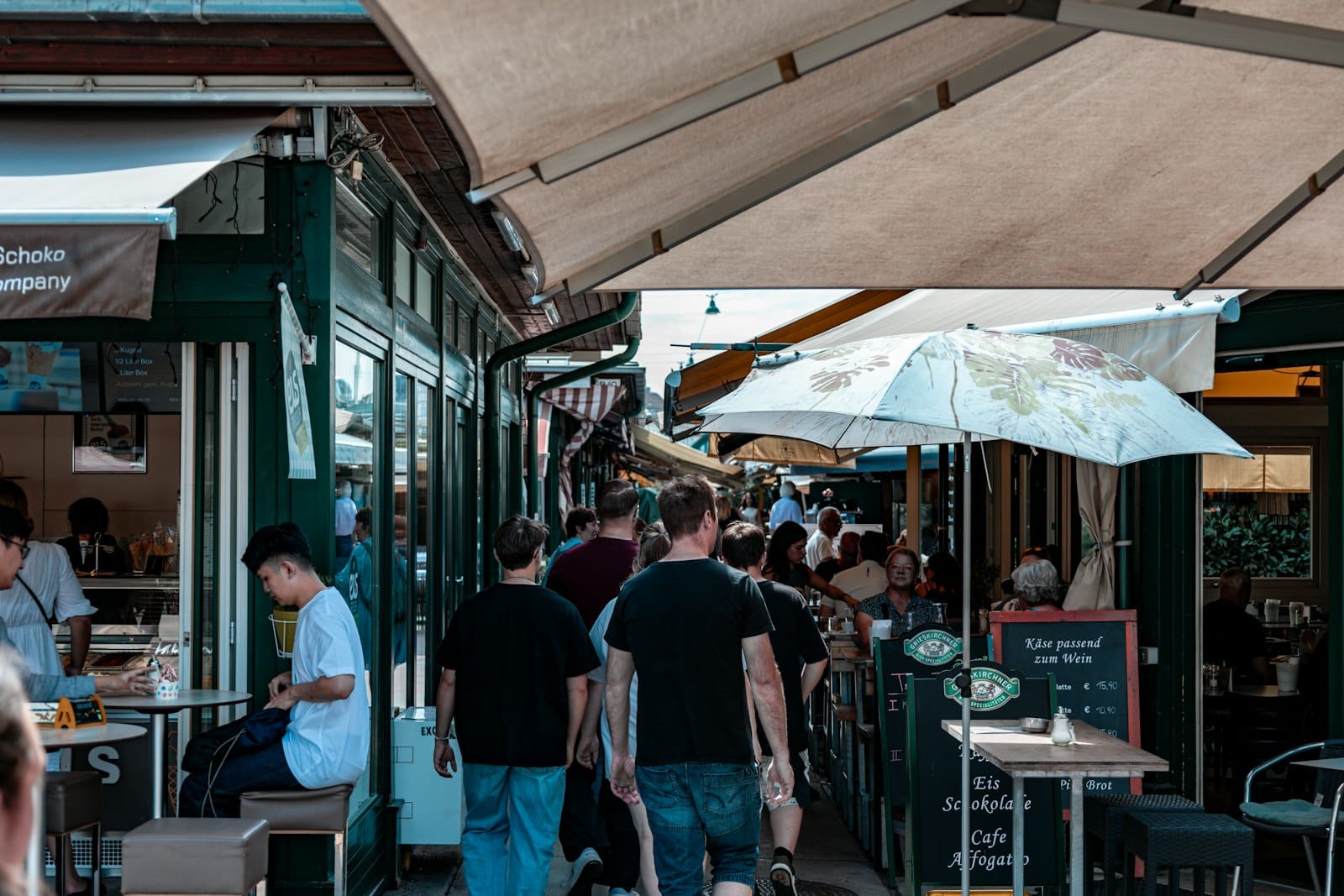 Vivace scena di mercato all'aperto al Naschmarkt di Vienna in una giornata di sole, con persone che passeggiano tra locali all'aperto e bancarelle ombreggiate.