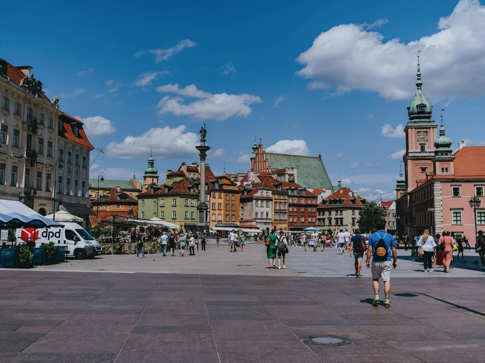 Vista vibrante da Praça da Cidade Velha de Varsóvia em um dia ensolarado, com coloridos edifícios históricos, pessoas caminhando e céu azul.