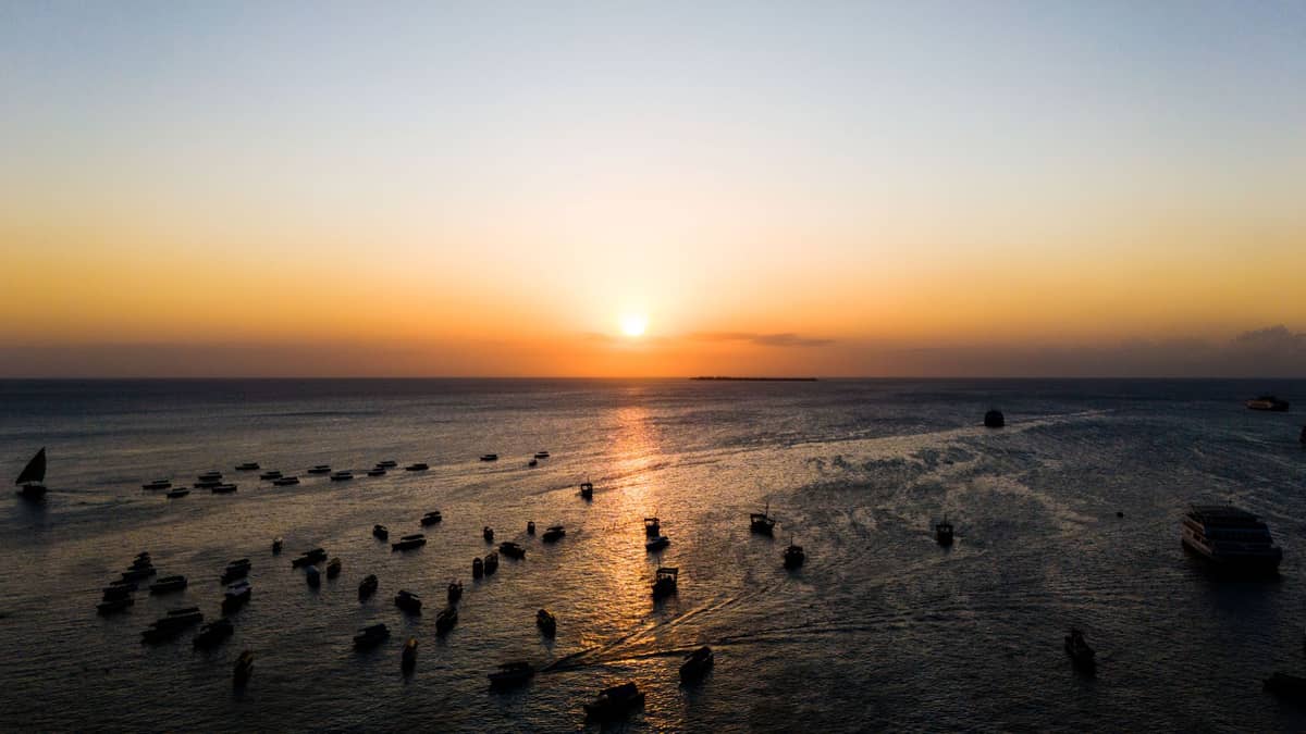 Foto de paisagem com muitos barcos no Oceano Índico ao pôr do sol com um céu dourado, típico das pitorescas noites costeiras de Zanzibar.