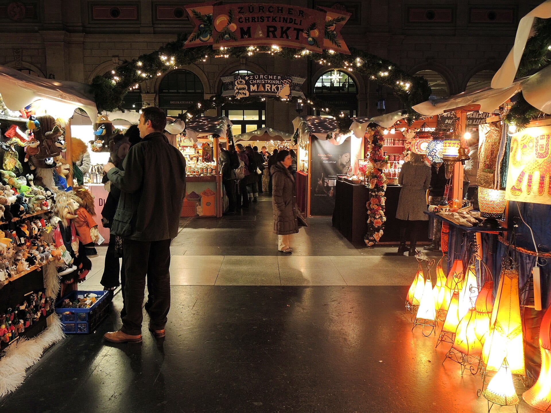 ตลาดคริสต์มาสในร่มของ Zurich Hauptbahnhof พร้อมแผงขายของที่ตกแต่งอย่างสวยงาม นักช้อปปิ้ง และไฟประดับในห้องโถงใหญ่ของสถานี