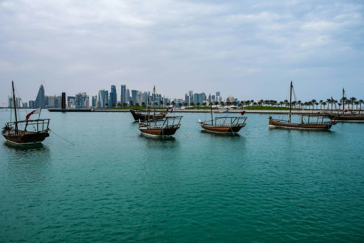 Traditionelle Dhau-Boote auf dem Wasser mit Dohas moderner West-Bay-Skyline im Hintergrund unter einem leicht bewölkten Himmel.