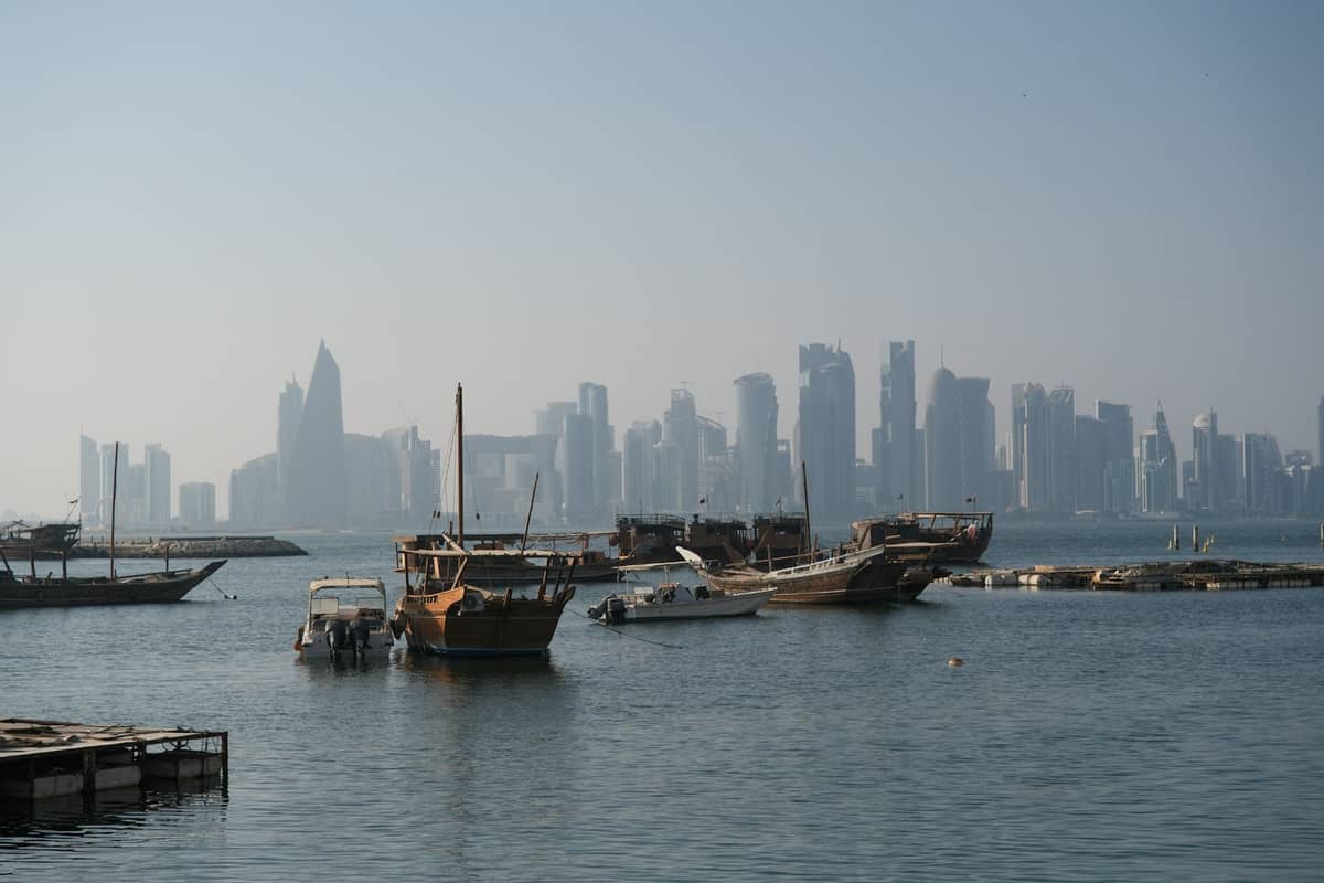 Traditionelle hölzerne Daus, die in der Bucht von Doha vertäut sind, mit der modernen Skyline von West Bay im Hintergrund, die über das Wasser sichtbar ist.