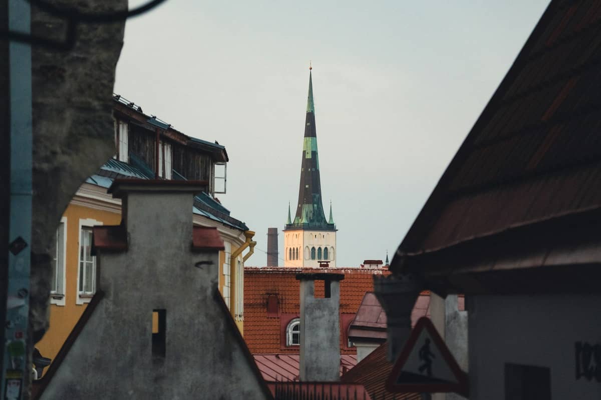 Nahaufnahme der Dächer der mittelalterlichen Altstadt von Tallinn mit einem markanten Kirchturm mit Spitze, der im Hintergrund über die Gebäude hinausragt.