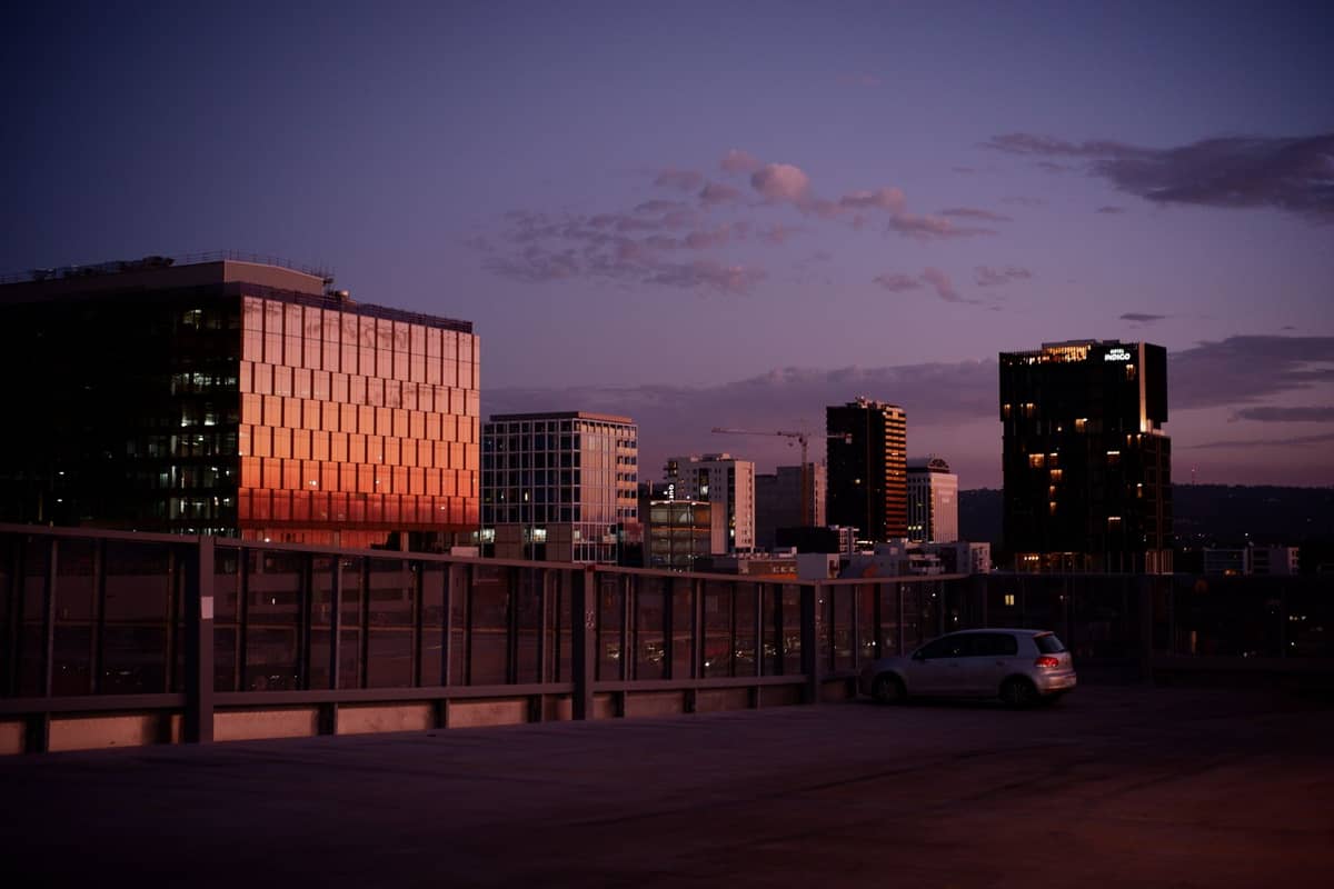 City skyline of Adelaide at dusk, viewed from a rooftop car park with reflections on modern glass buildings and a purple sky.
