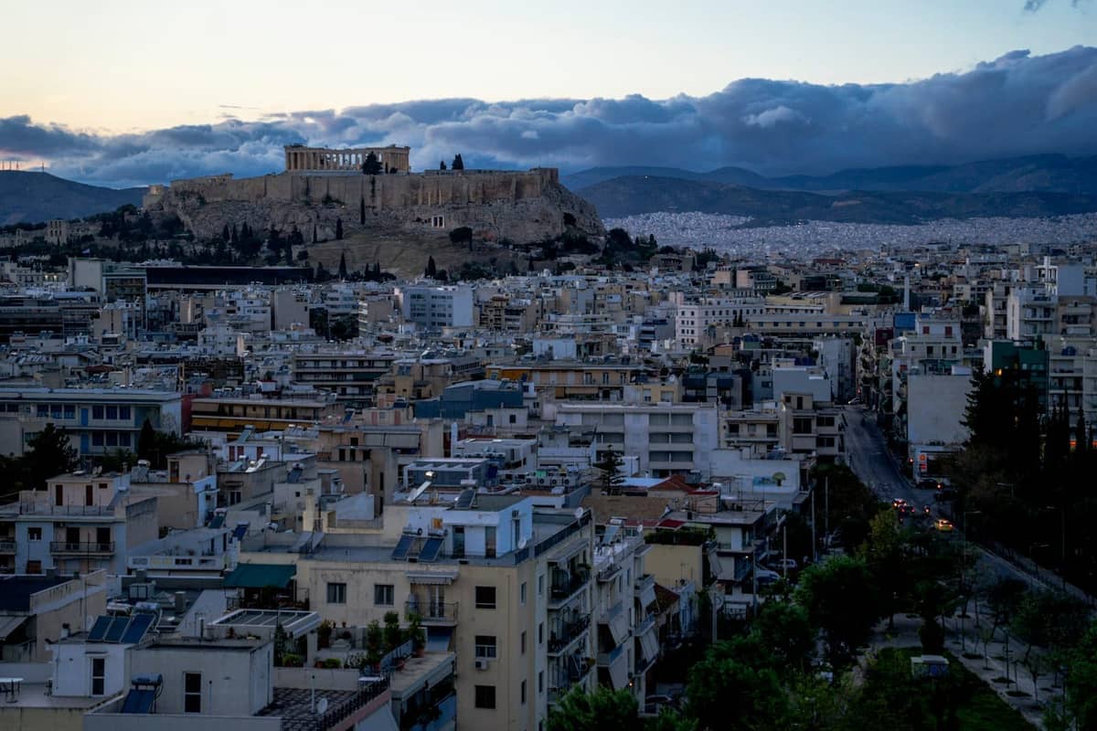 Stadtpanorama von Athen in der Dämmerung mit Dachterrassen-Aussichten und der beleuchteten Akropolis auf einem Hügel im Hintergrund, städtische Gebäude im Vordergrund.