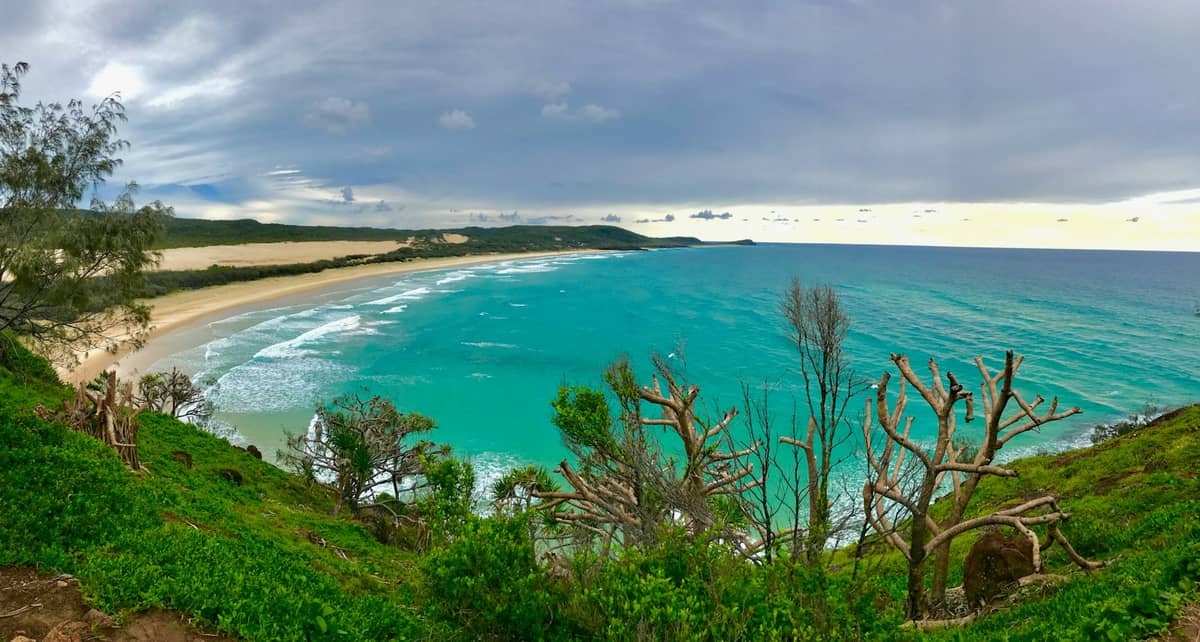 Mirador costero elevado con vistas al océano turquesa y playa de arena, probablemente North Stradbroke Island o Moreton Island cerca de Brisbane bajo un cielo nublado.
