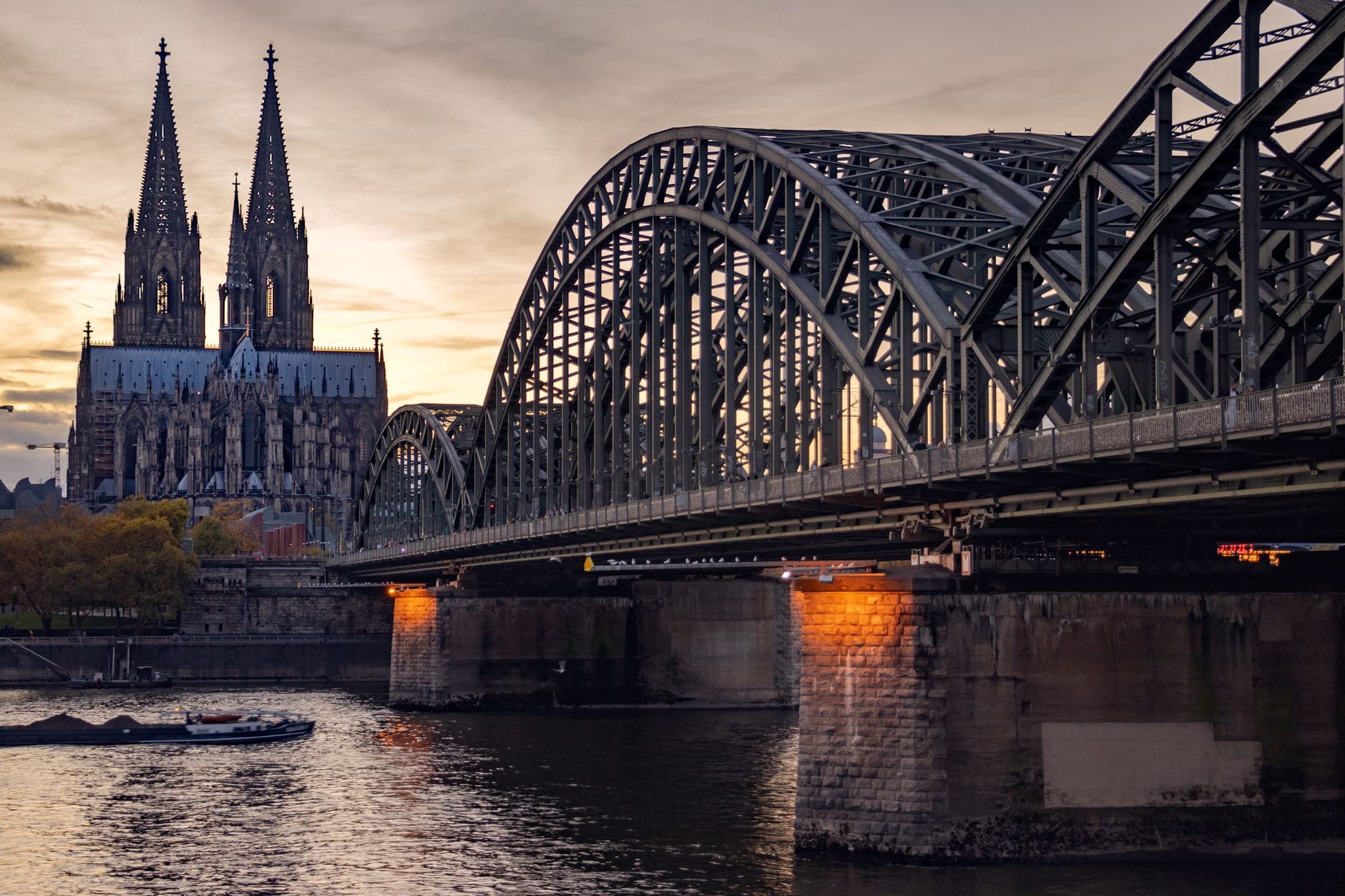 มหาวิหารโคโลญและสะพาน Hohenzollern ที่มองเห็นข้ามแม่น้ำไรน์ในยามเย็น เน้นจุดชมวิวฟรีที่เป็นสัญลักษณ์