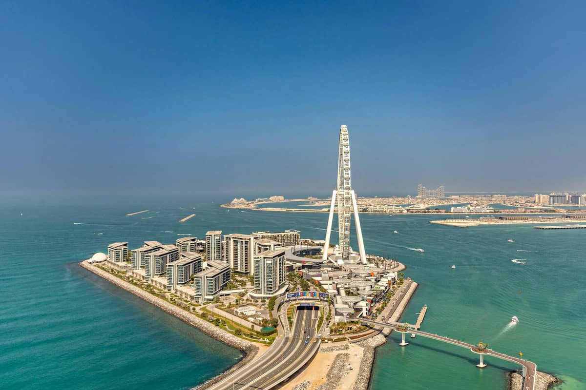 Luftaufnahme des Riesenrads Ain Dubai und des umliegenden Hafenbereichs mit türkisfarbenem Meer unter einem klaren blauen Himmel.