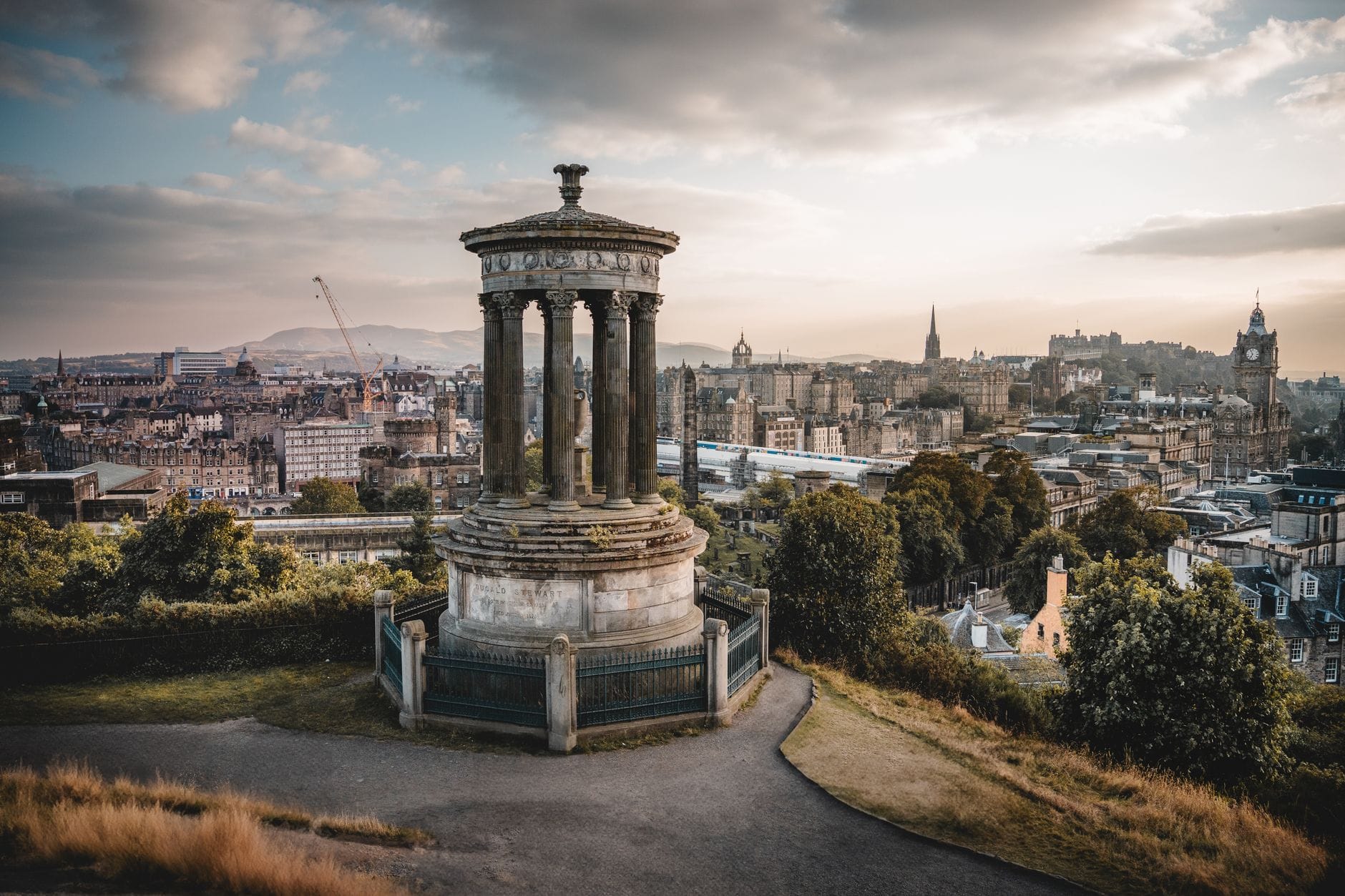 Le Monument Dugald Stewart sur Calton Hill surplombant la skyline d'Édimbourg au crépuscule, avec le Château d'Édimbourg et les monuments de la ville visibles au loin.
