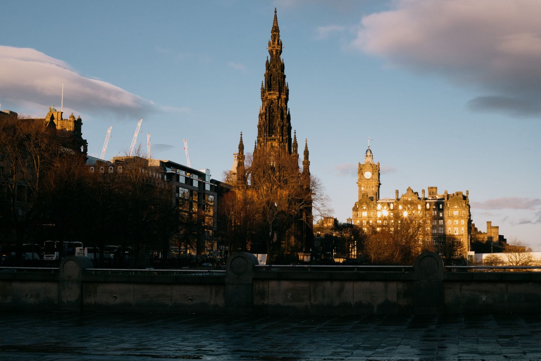 Vue panoramique du Scott Monument et de la tour de l'horloge du Balmoral Hotel depuis le niveau de la rue, baignés dans la lumière du soir, avec l'architecture caractéristique de la ville d'Édimbourg.