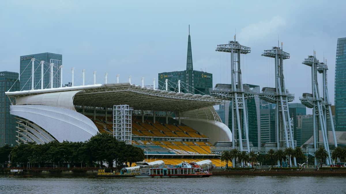 Guangzhou stadium with distinctive modern roof, yellow seats, and dramatic skyline background seen from across the Pearl River.