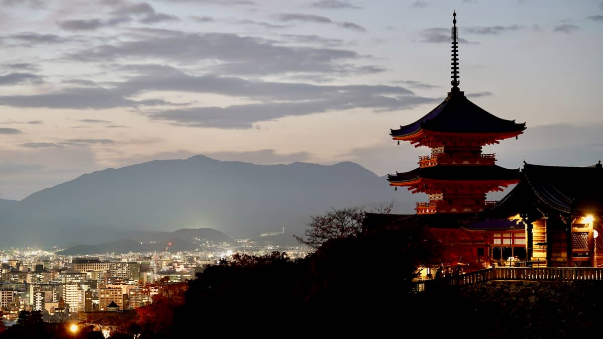 Kiyomizu-dera temple stage overlooking Kyoto city at dusk with mountains in the background and city lights starting to glow.