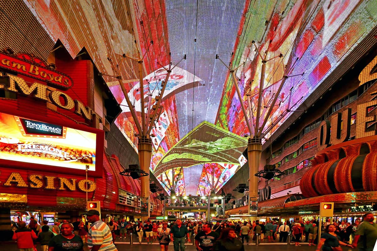 ฝูงชนเดินอยู่ใต้หลังคา Fremont Street Experience ที่สดใสและส่องสว่าง โดยมีคาสิโนและป้ายนีออนเรียงรายทั้งสองข้างในตัวเมืองลาสเวกัส