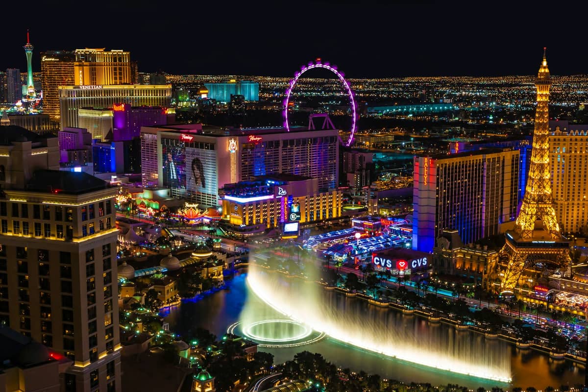 A stunning night view of the Las Vegas Strip featuring the Bellagio fountains, Eiffel Tower replica, High Roller observation wheel, and Stratosphere Tower in the distance.
