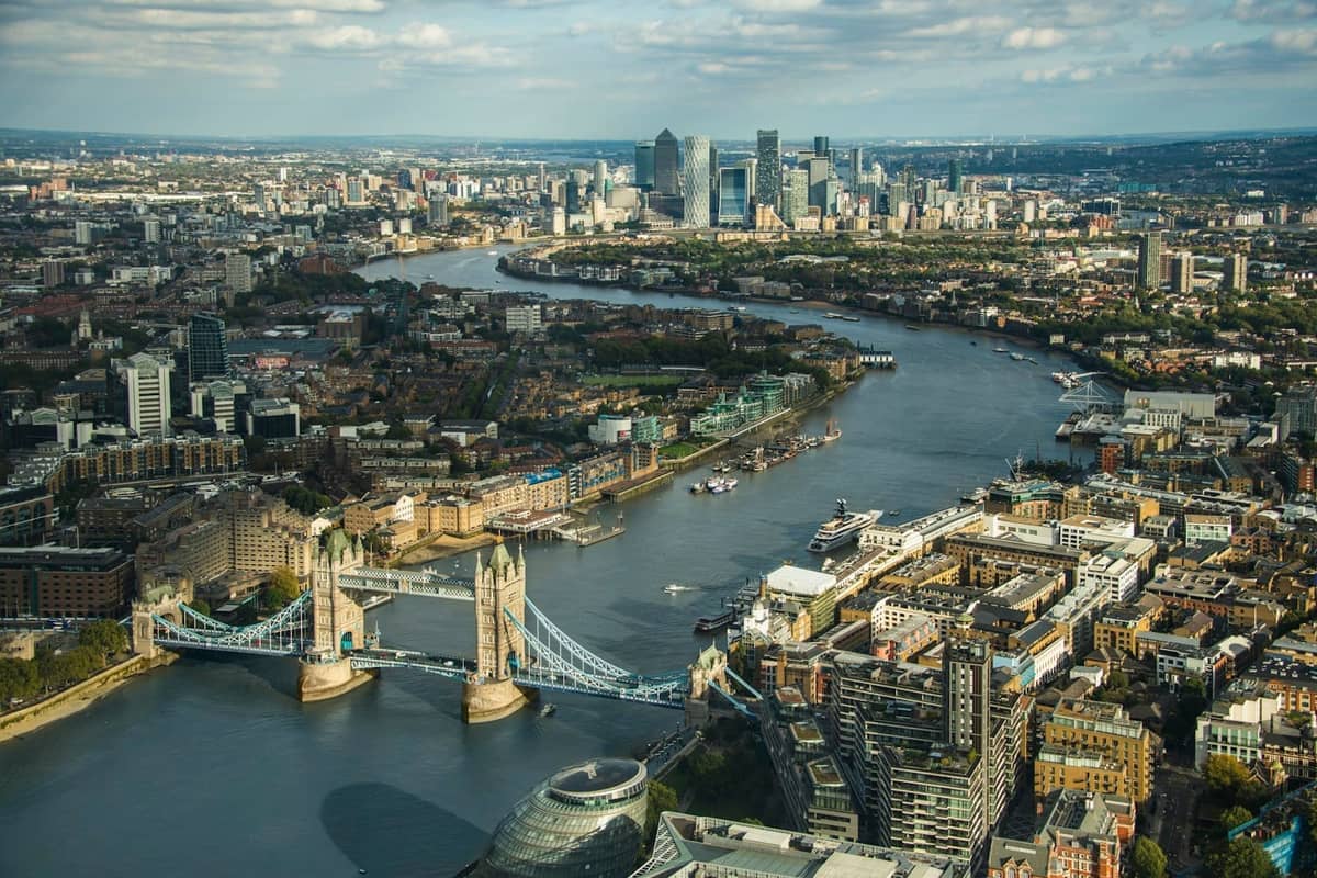 Vista aérea da Tower Bridge sobre o rio Tâmisa, com o horizonte de Londres e a margem do rio bem visíveis.