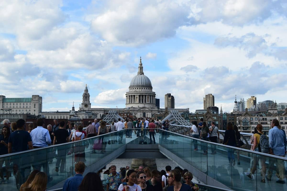Multidões atravessando a Millennium Bridge em direção à Catedral de St Paul's sob um céu claro e parcialmente nublado no centro de Londres