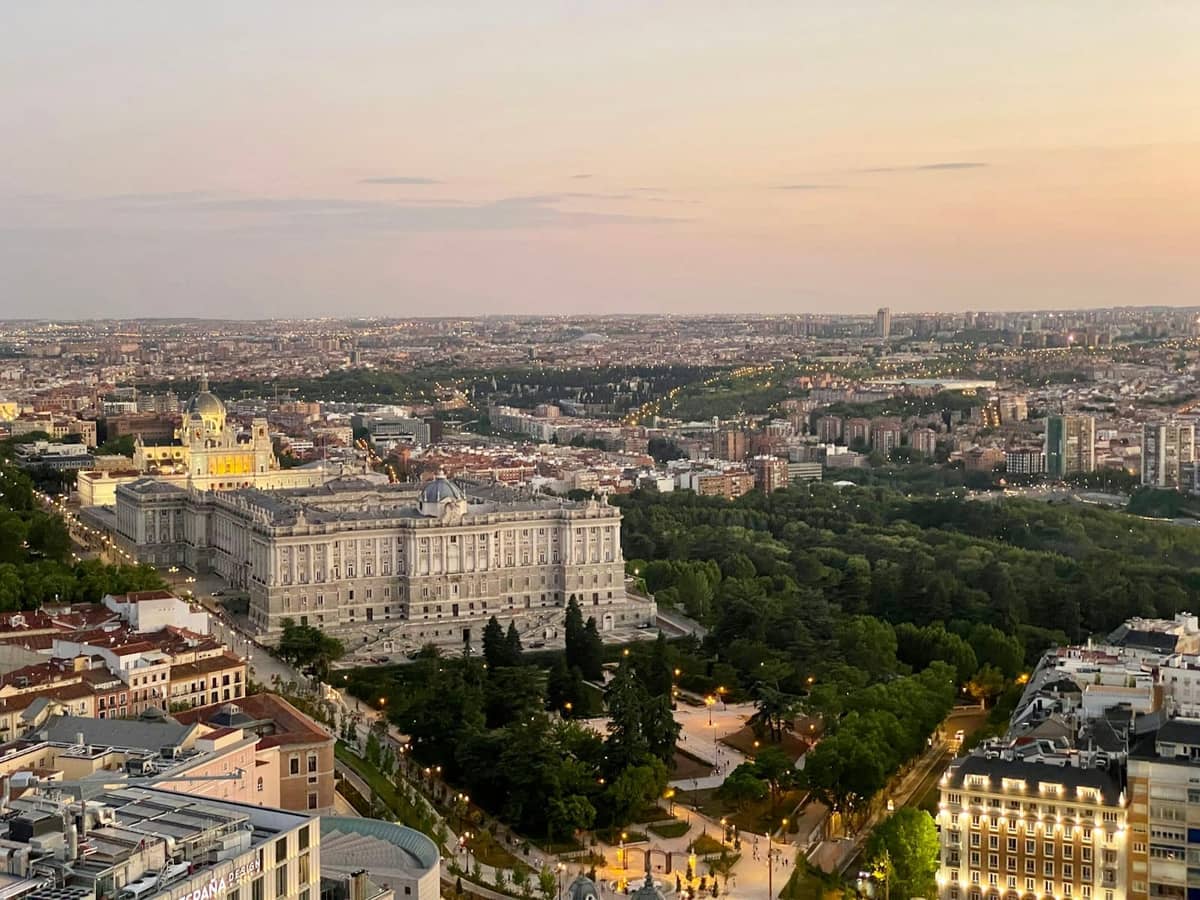 Panoramiczny widok na Madryt z Palacio Real i rozległymi terenami zielonymi o zachodzie słońca, ukazujący klasyczny punkt widokowy na miasto.