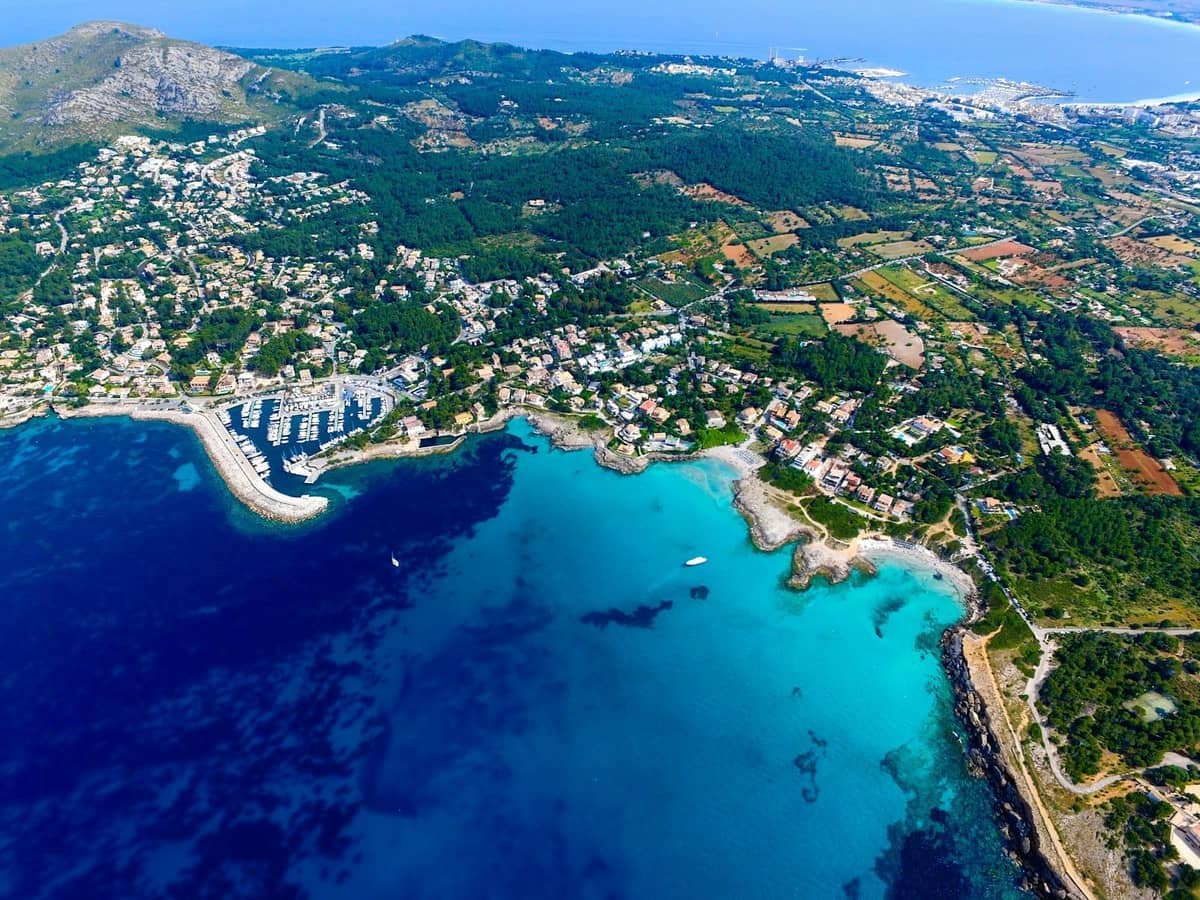 Vista aerea della costa di Mallorca con acque turchesi, marine e lussureggianti aree verdi nell'entroterra, che mostrano l'isola dall'alto.
