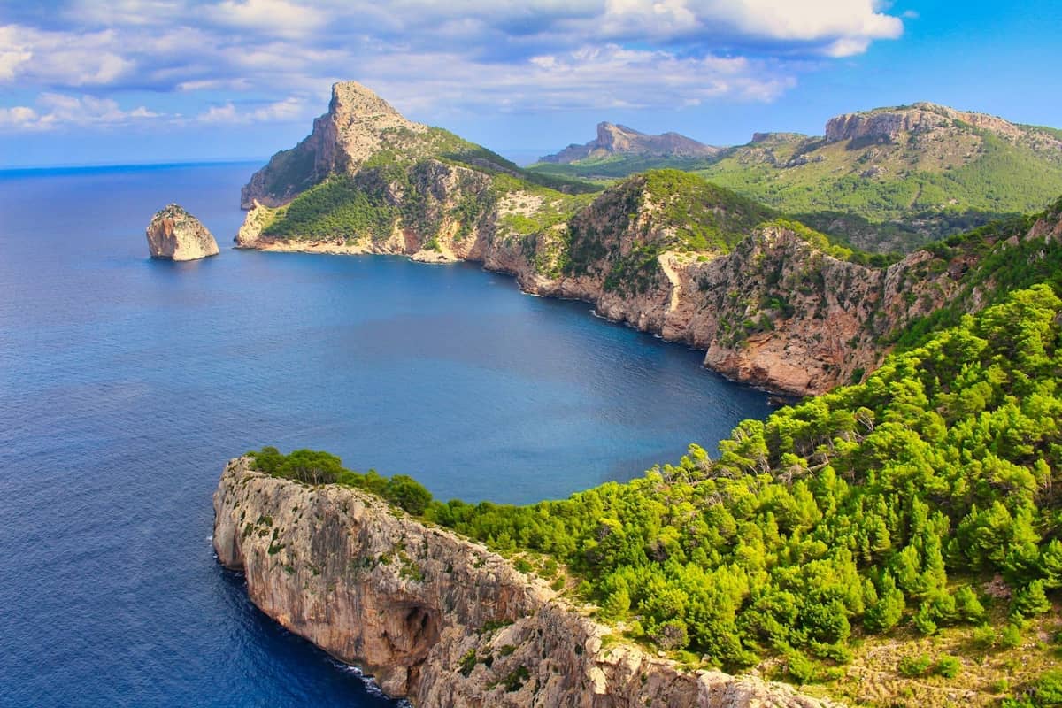 Vista spettacolare sulla drammatica costa settentrionale di Mallorca con scogliere, mare blu profondo, foreste di pini e promontori suggestivi sotto un cielo parzialmente nuvoloso.