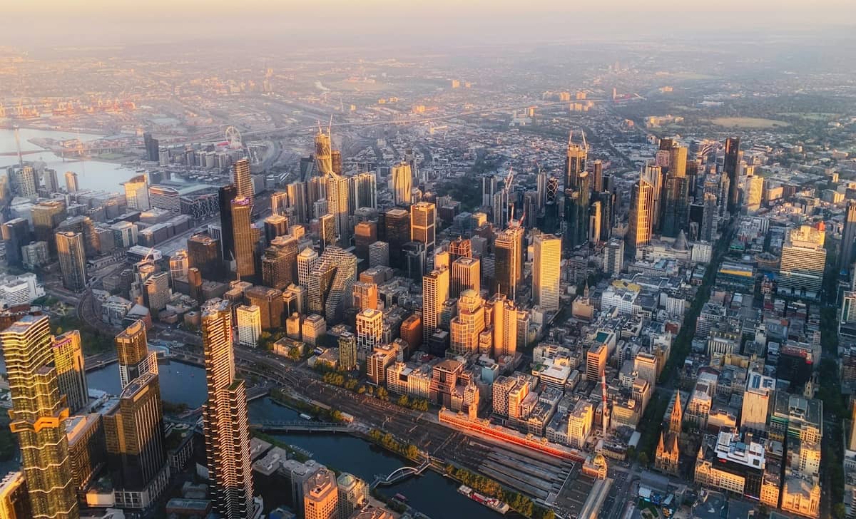 Vista aérea del CBD de Melbourne al amanecer con rascacielos, el río Yarra y la extensa trama urbana bajo la luz dorada de la mañana.
