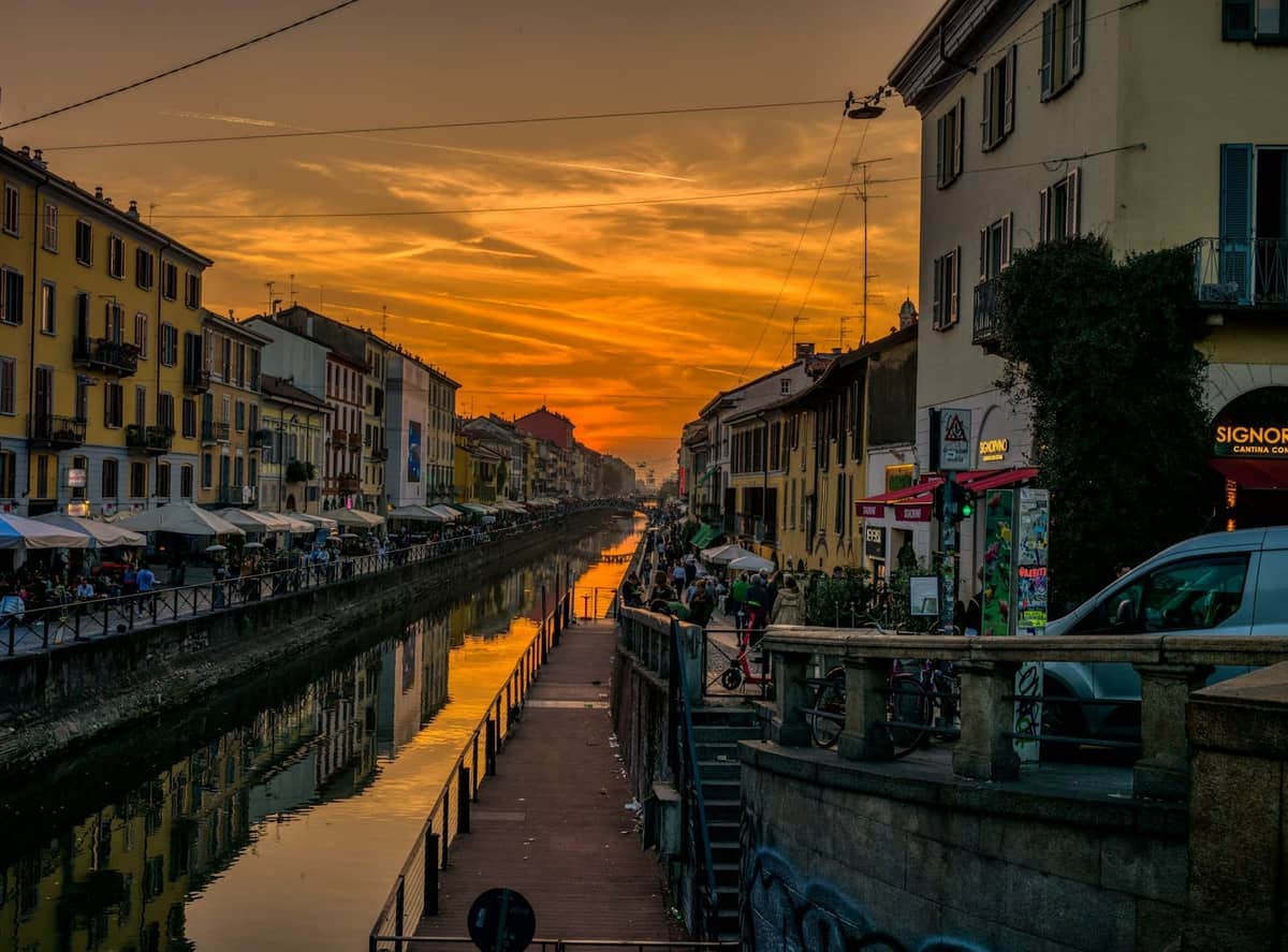 Zachód słońca nad kanałem Naviglio Grande w Mediolanie z odbiciami, kawiarniami i kolorowymi budynkami wzdłuż wody.