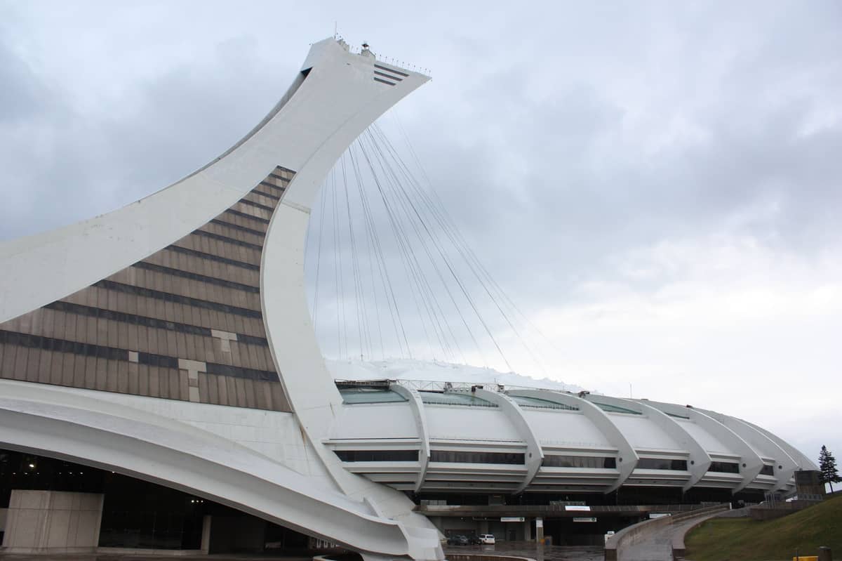 Widok na Wieżę Olimpijską w Montrealu i konstrukcję stadionu w pochmurny dzień, prezentujący ikoniczną pochyloną wieżę widokową.
