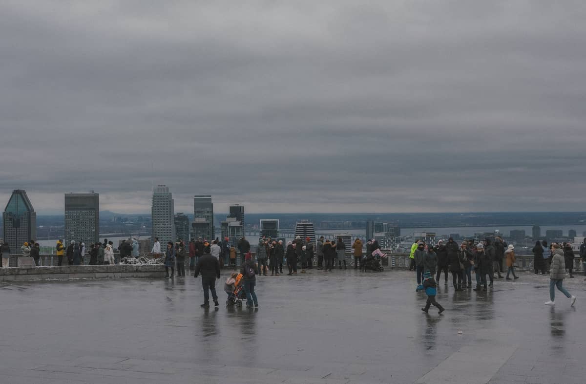 Zwiedzający zbierają się przy Kondiaronk Belvedere na Mont Royal, podziwiając panoramę Montrealu w pochmurny dzień.