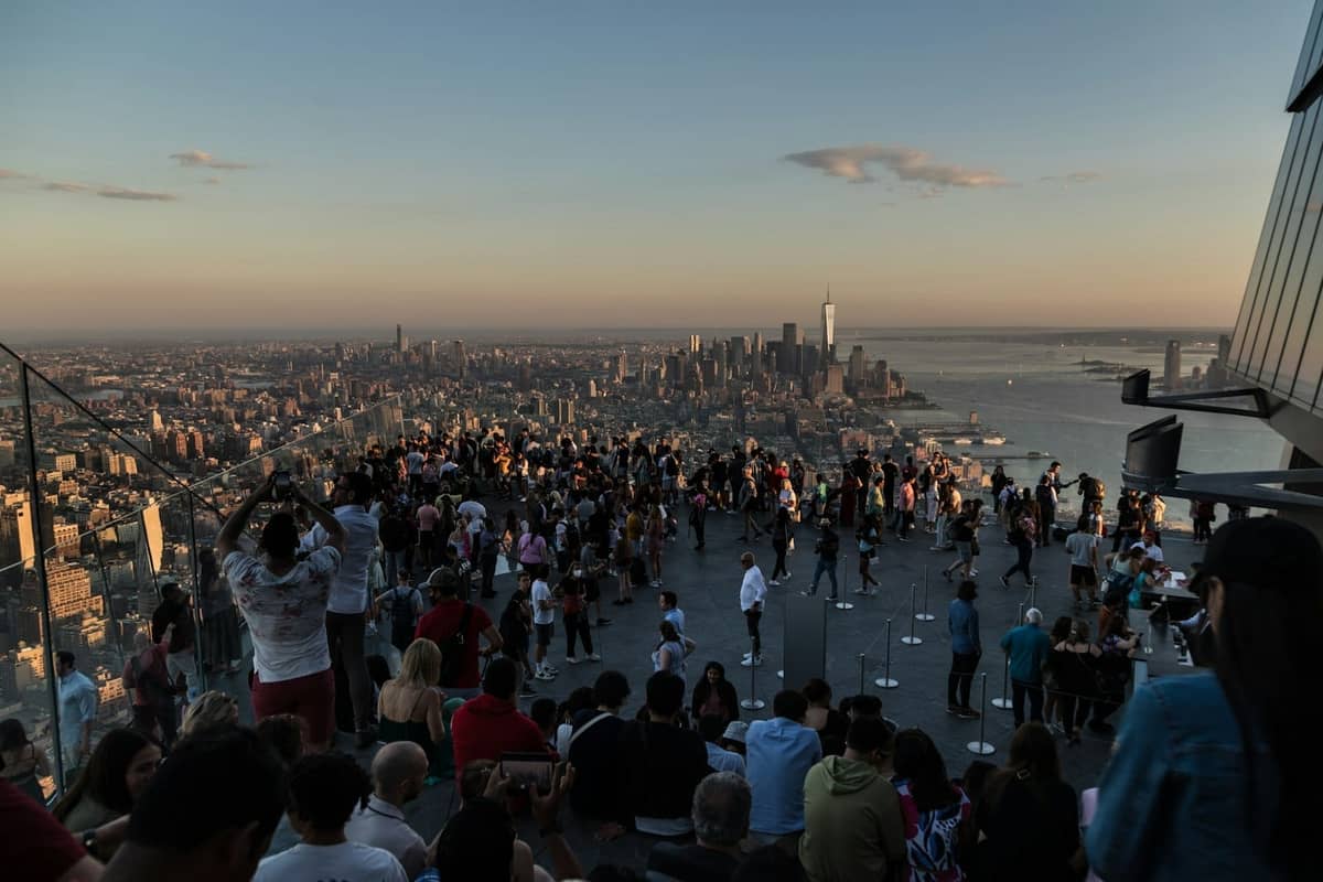 Menschenmenge auf einer Aussichtsplattform in New York City bei Sonnenuntergang, mit einem weiten Blick auf die Skyline und den Fluss.