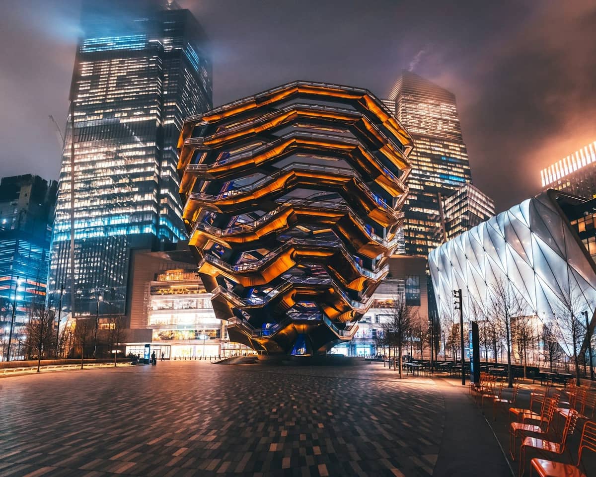 Nachtansicht von The Vessel, einer ikonischen wabenförmigen Struktur, umgeben von Wolkenkratzern in Hudson Yards, New York City.