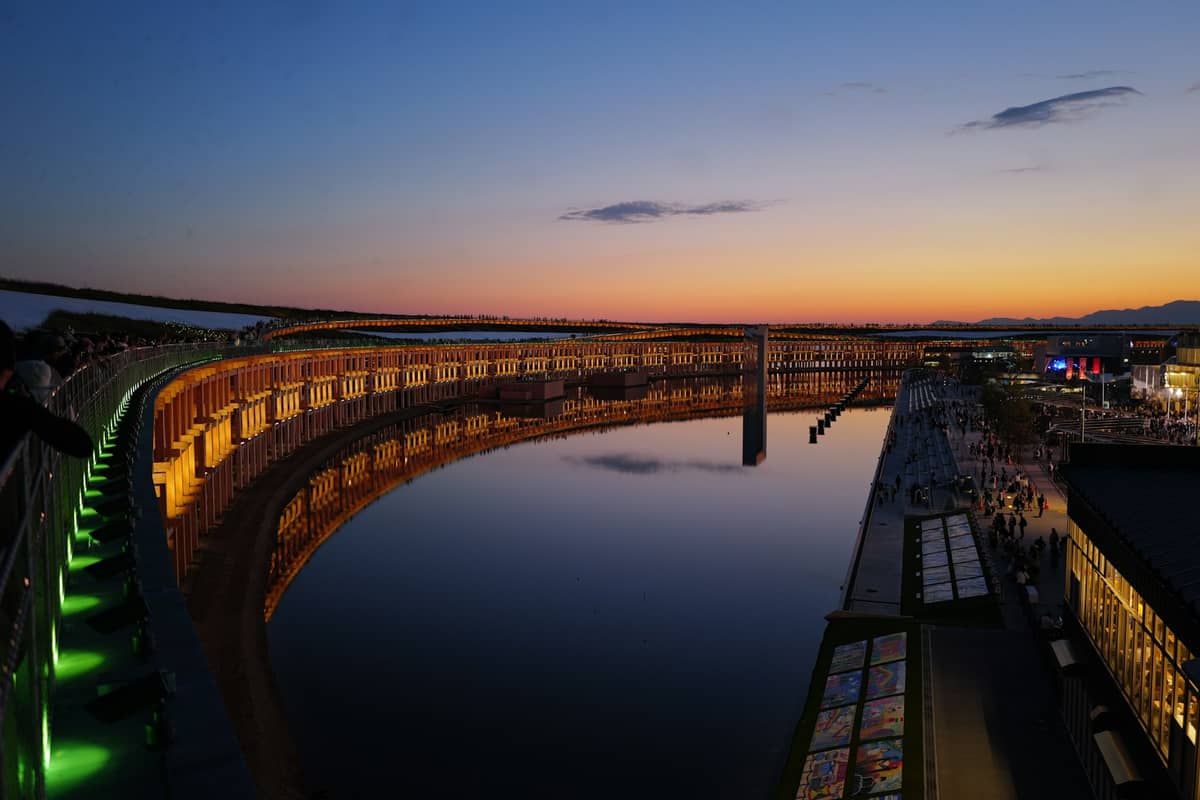 View of a large waterfront promenade curving along open water at sunset with buildings and people enjoying the bay in Osaka.