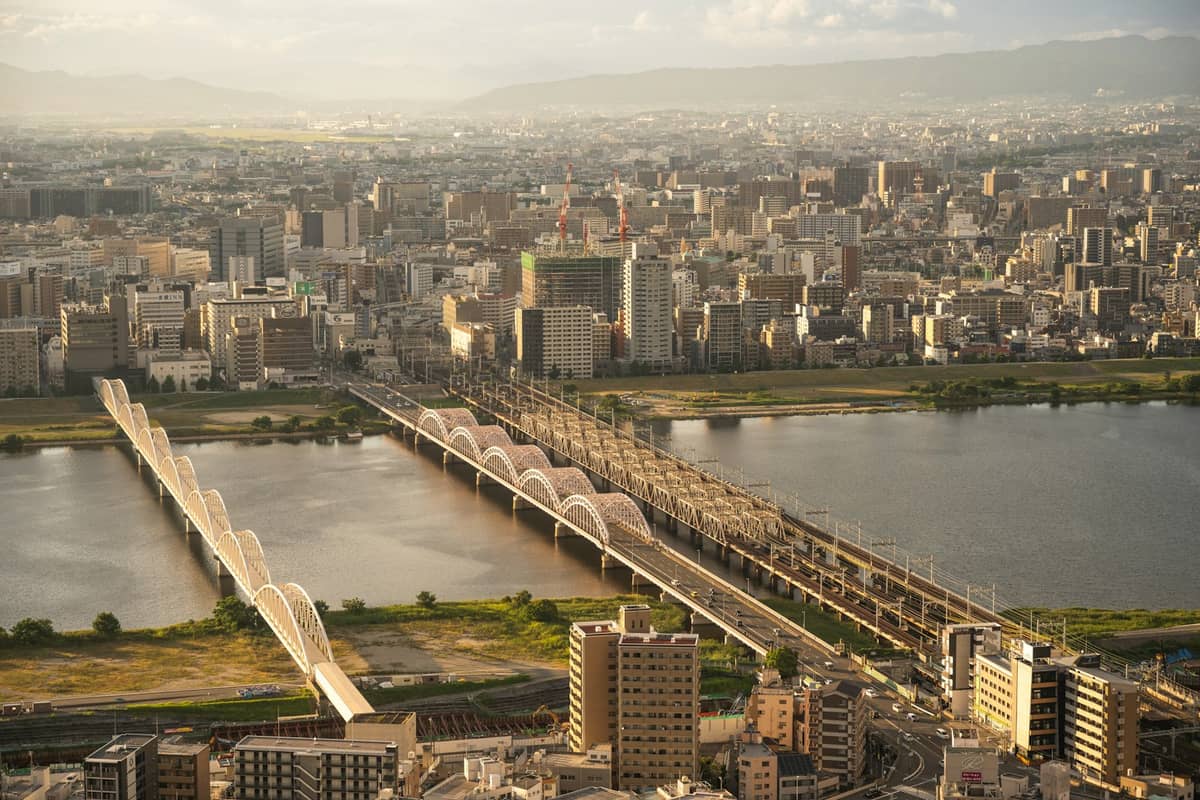 A panoramic view of central Osaka showing wide city sprawl, river, and arched bridges, as seen from a famous high-rise observatory.