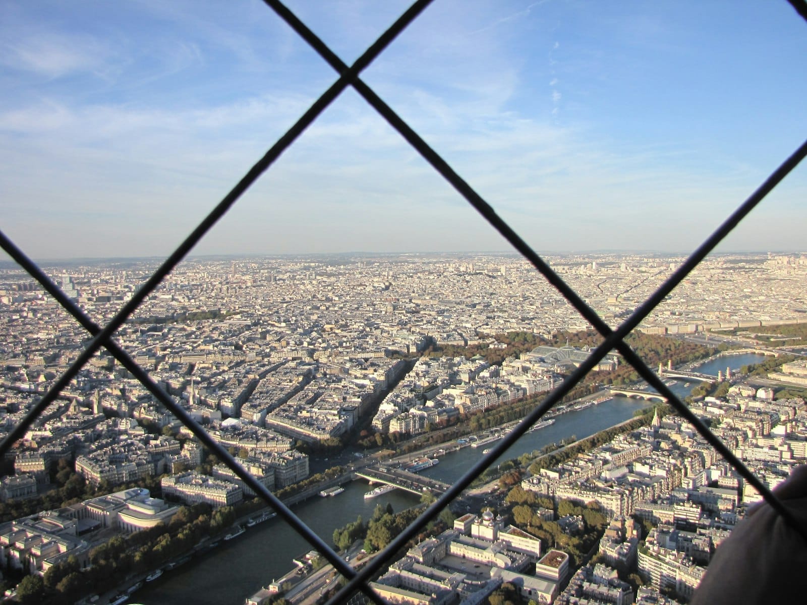 Panoramablick auf die Skyline von Paris von einem erhöhten Aussichtspunkt aus, gesehen durch einen kreuzförmigen Metallzaun mit dem sichtbaren Fluss Seine darunter.