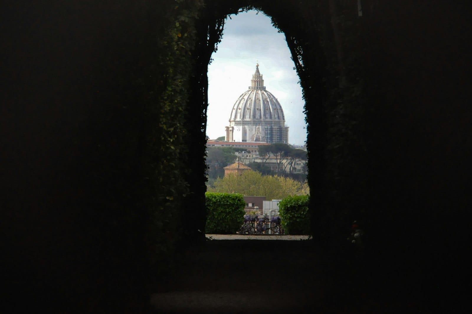 A view of St. Peter’s dome perfectly framed through the famous Aventine Keyhole in Rome, with leafy archway borders and a distant cityscape.