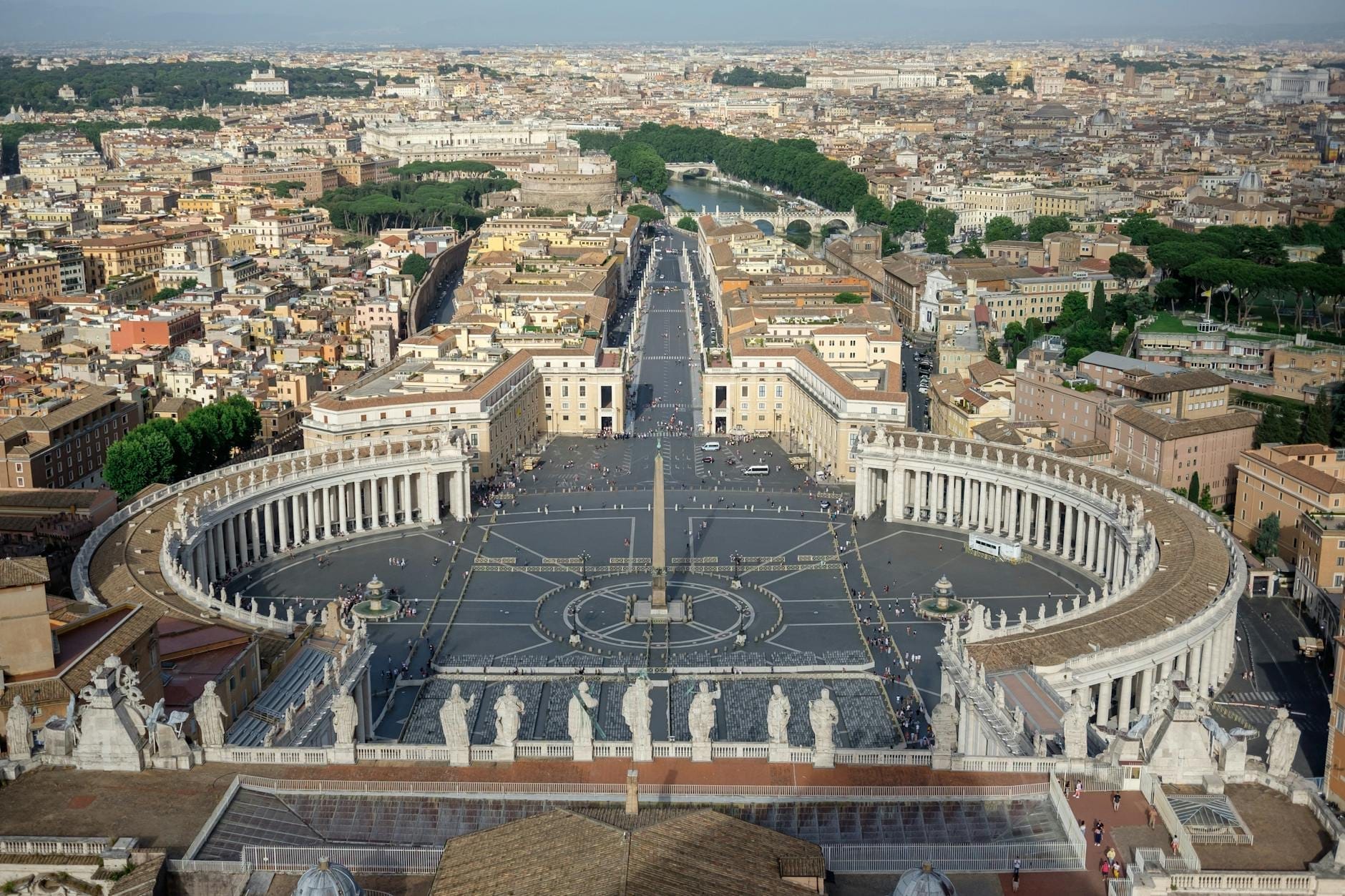 Wide, clear view from the top of St. Peter's Basilica, looking over St. Peter's Square and the city of Rome under a bright sky.