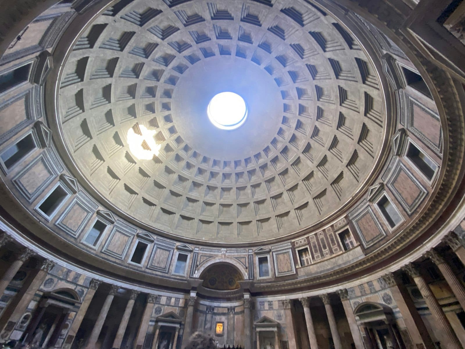 Wide view from inside the Pantheon, showing its iconic dome, oculus, and architectural details illuminated by sunlight.