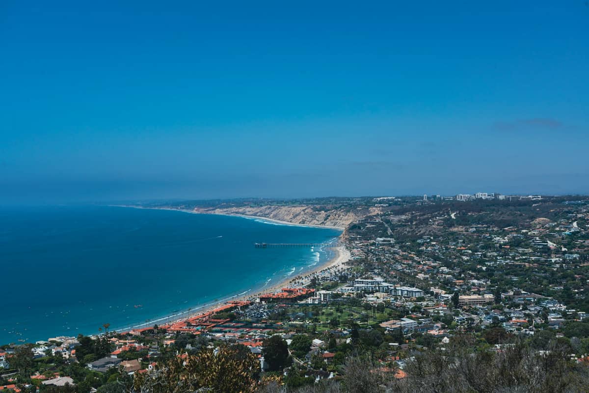 Weite Luftaufnahme der Küste von La Jolla in San Diego mit Klippen, Pazifik und Stadtsilhouette unter strahlend blauem Himmel.
