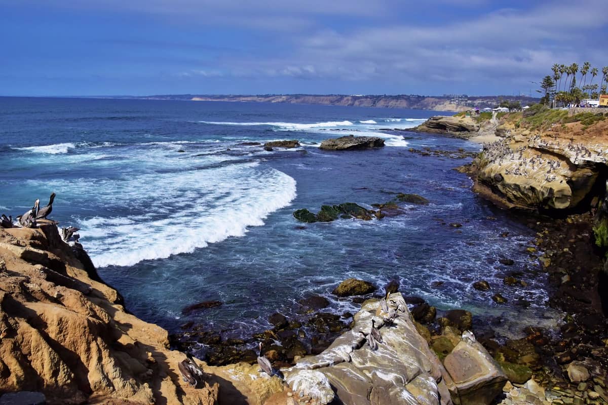 วิวกว้างของหน้าผาชายฝั่ง La Jolla พร้อมคลื่นซัดฝั่ง หินขรุขระ และแนวชายฝั่งที่อยู่ไกลออกไปใต้ท้องฟ้าสดใส