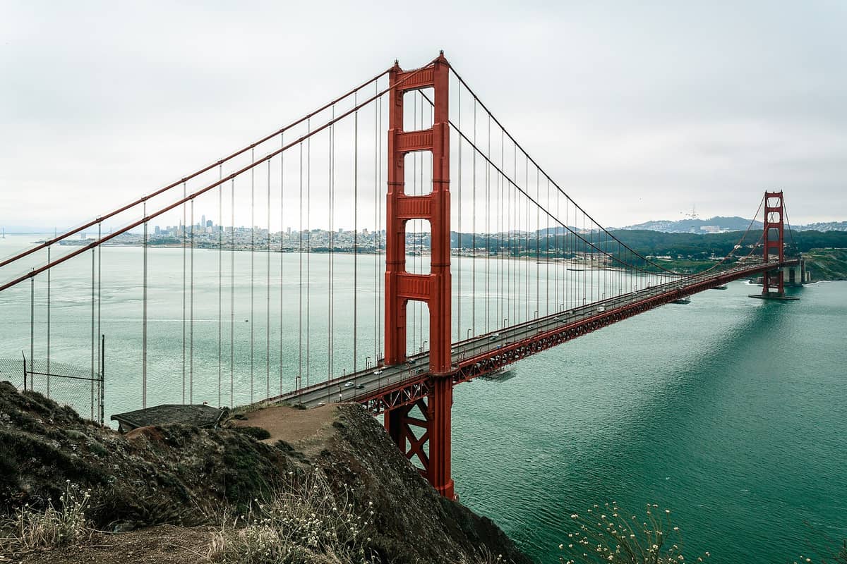 Klassische Landschaftsansicht der Golden Gate Bridge von den Marin Headlands aus, mit der Skyline von San Francisco und der blaugrünen Bucht im Hintergrund.