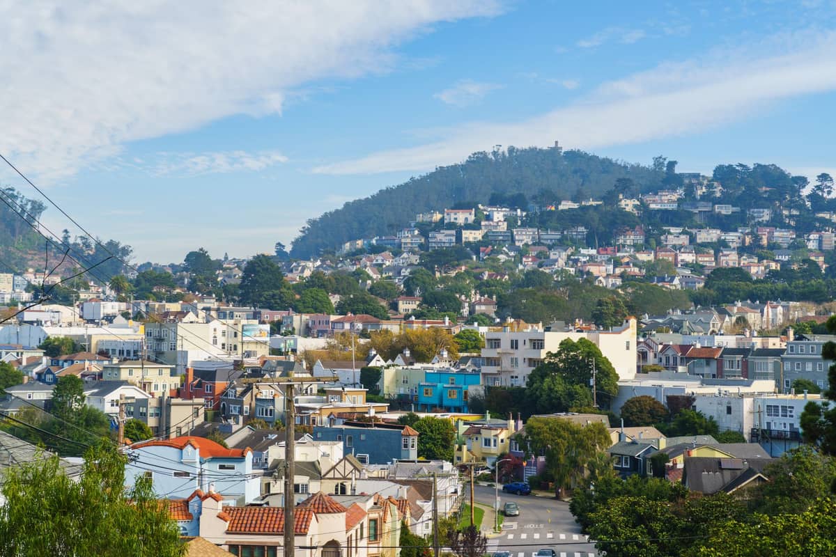 Häuser in einem Wohnviertel in San Francisco mit einem grünen Hügel im Hintergrund unter einem blauen Himmel mit Wolken.