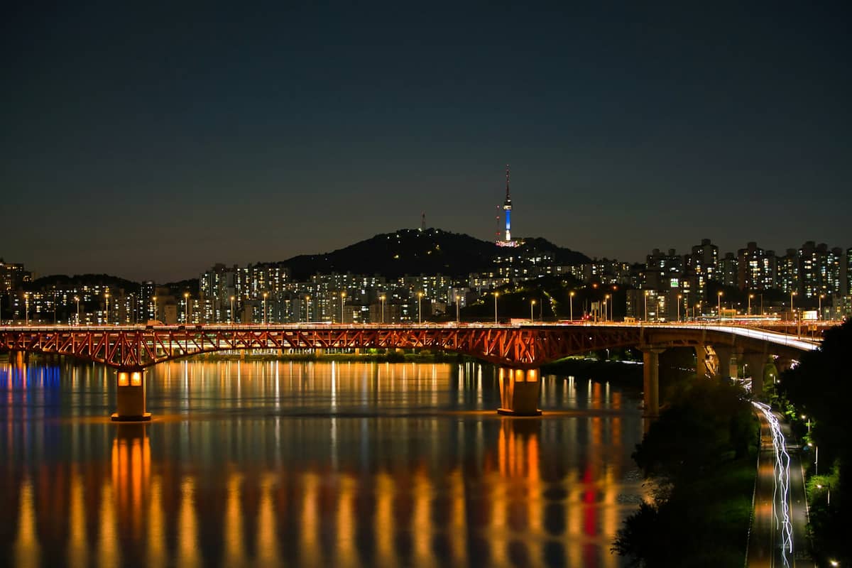 Vista noturna do horizonte de Seul com a N Seoul Tower iluminada em uma colina, luzes brilhantes da cidade refletidas no Rio Han.