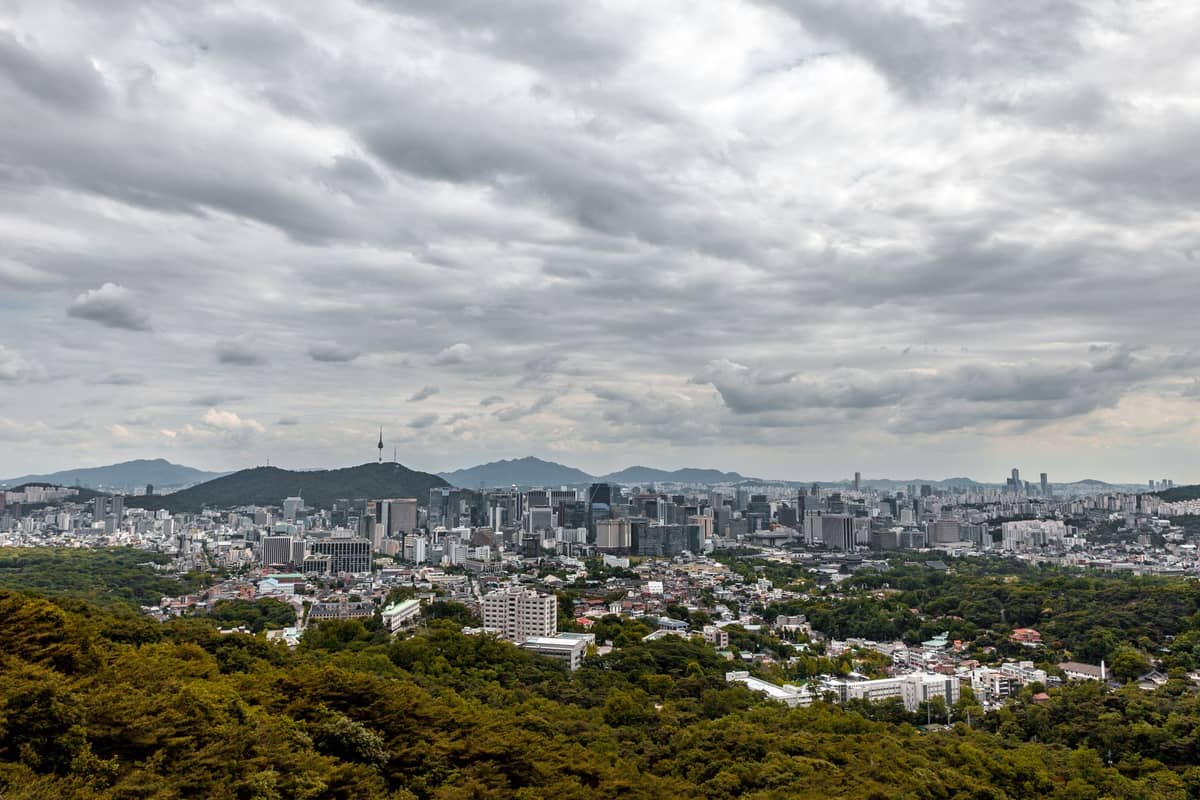 Vista panorâmica do centro de Seul a partir de um morro, mostrando o skyline da cidade, a Torre Namsan ao fundo e um céu dramático com nuvens.