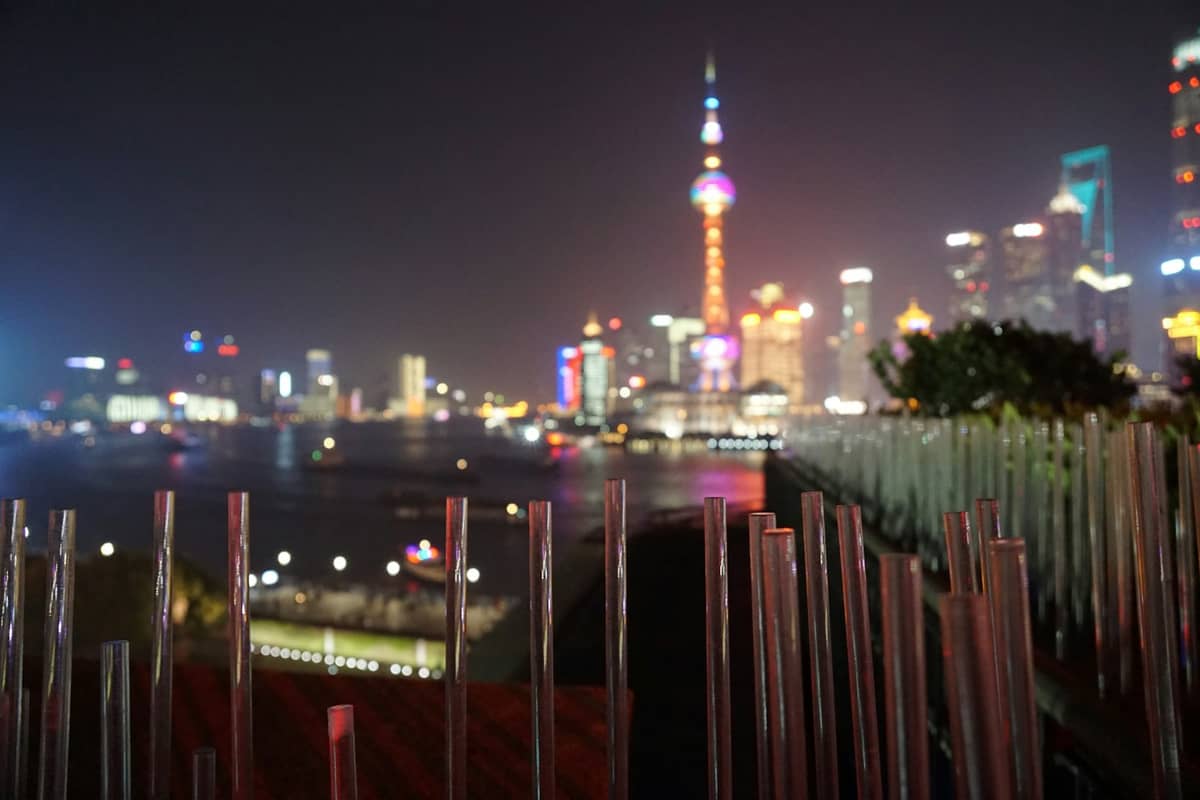 Pemandangan malam yang buram dari cakrawala Shanghai dari bar atap dengan Oriental Pearl Tower yang menyala di kejauhan.