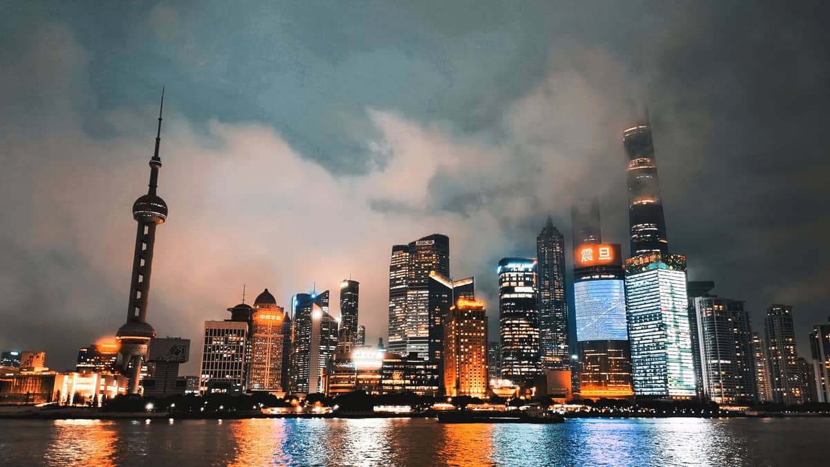 Nächtlicher Blick auf die Shanghaier Skyline mit dem Oriental Pearl Tower und dem Shanghai Tower, beleuchtet und im Huangpu-Fluss gespiegelt, vom Bund aus gesehen.